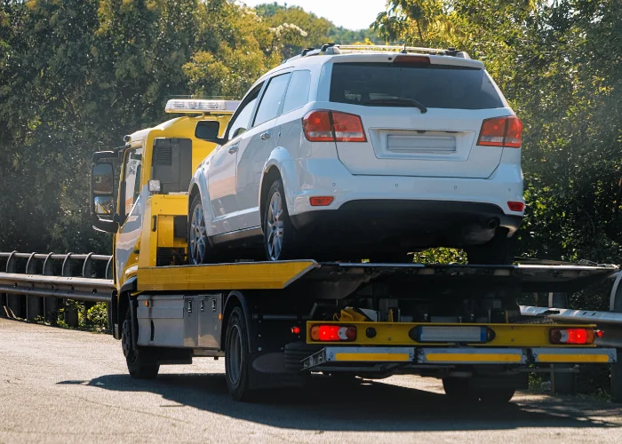 Una grúa de color amarilla, esta transportando un vehículo de color gris sobre su plataforma en una carretera.